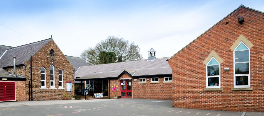 photograph of the front of Wistow School and the playground on a day with blue skies